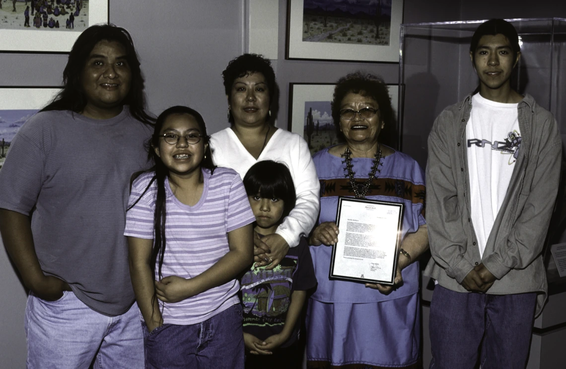 A family of 6 stand and smile at the camera. From left to right there is an adult male, a teenage girl, a young boy, two adult women, and a teenage boy.