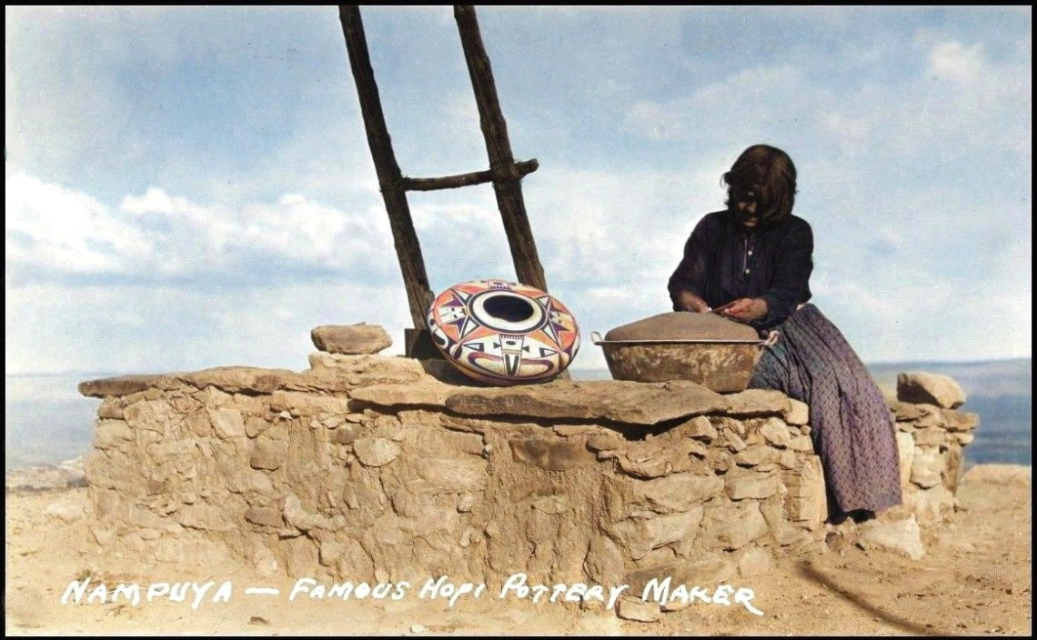 a Hopi woman sits on a rock wall forming a large, wide-shouldered jar using a large metal basin as a base