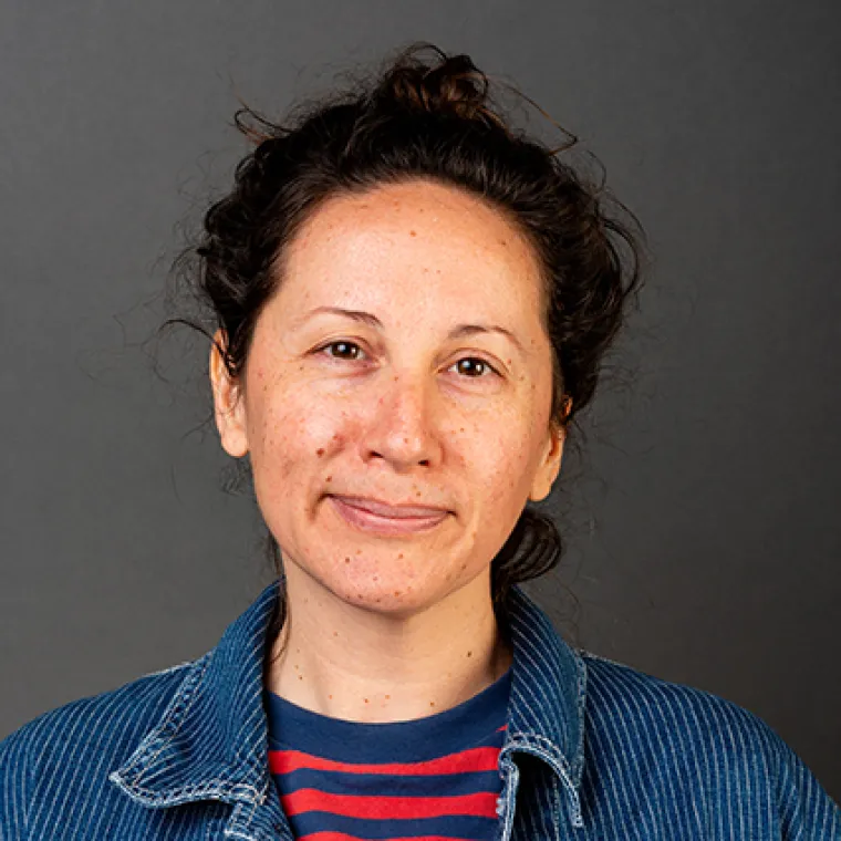 woman wearing her brown hear up and wearing a denim jacket over a blue and red striped top